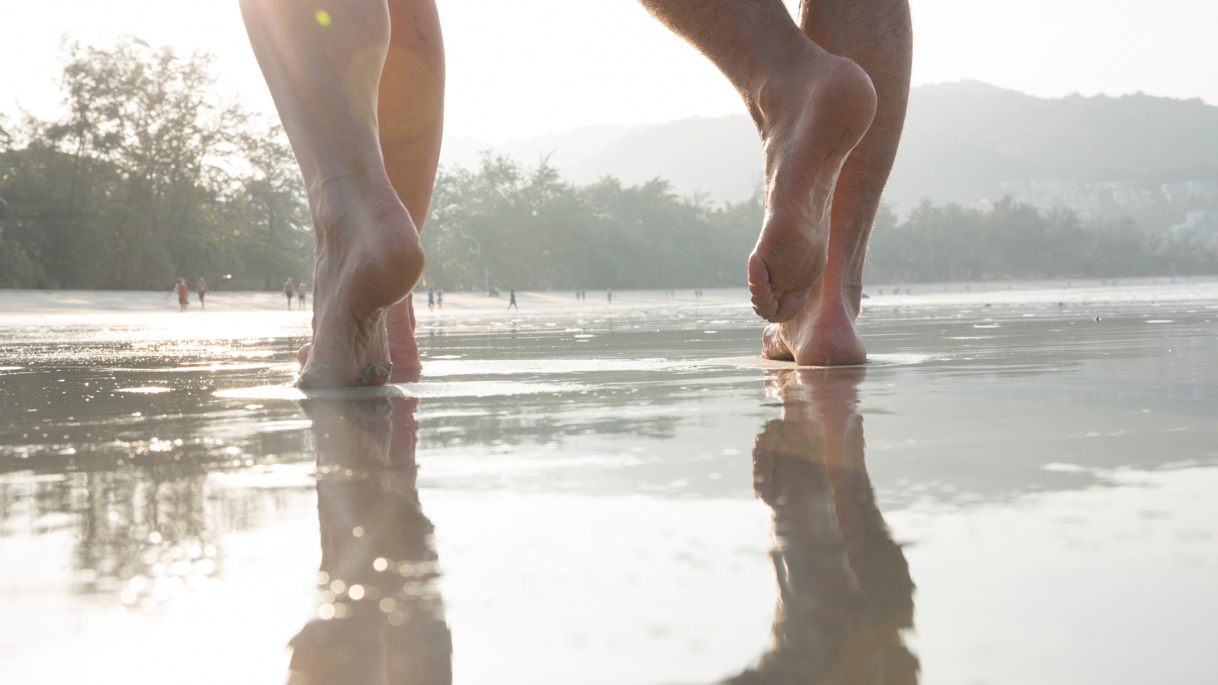 Close up on feet of two people walking barefoot through water soaked sand